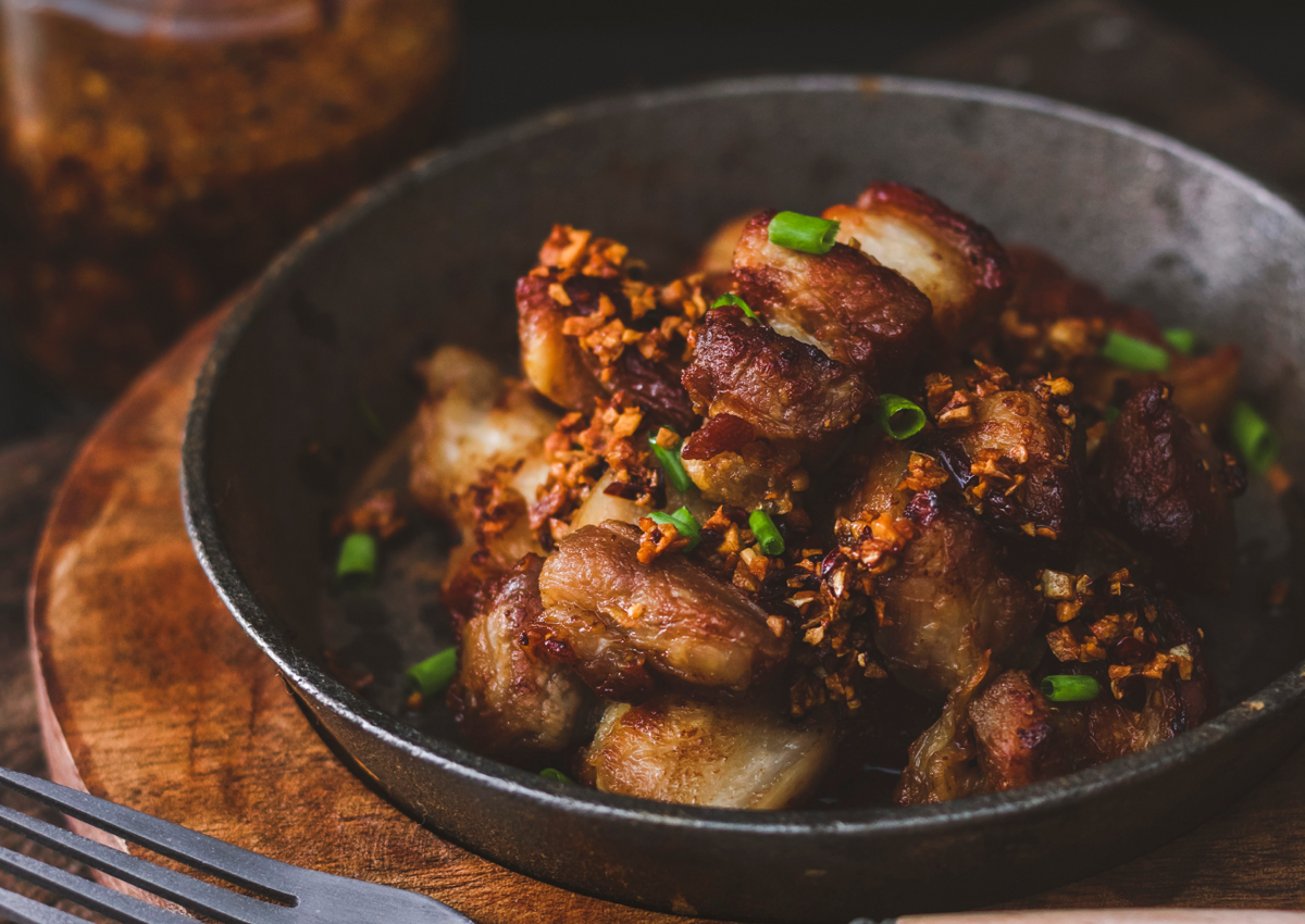 Crispy pork belly bites with garlic and green onions in a cast iron skillet