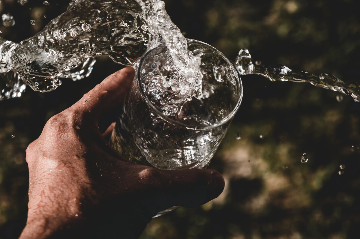 Hand holding a glass under a stream of running water with splashing droplets