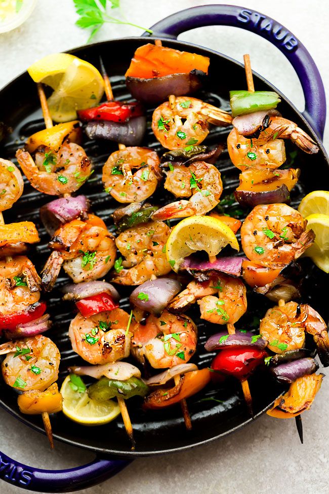 Shrimp skewers with peppers onions and lemon wedges on a round grill pan