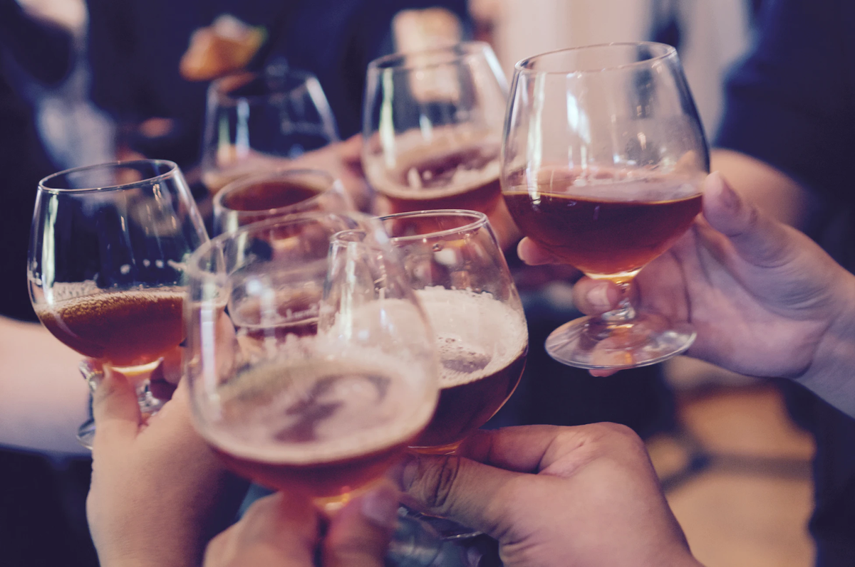 Group of friends clinking stemmed glasses filled with dark drinks in a toast