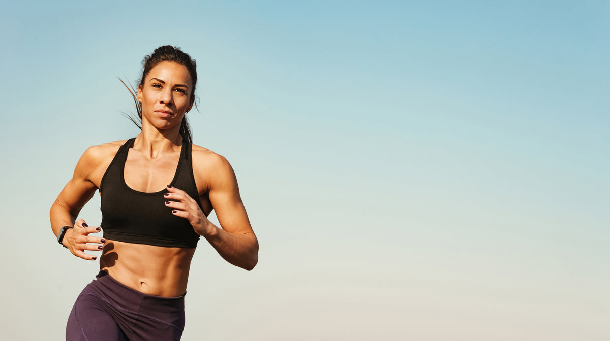 Athletic woman in a black sports bra jogging outdoors under a clear blue sky.