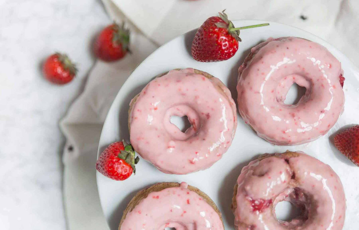 Pink strawberry donuts on a white plate with fresh strawberries nearby