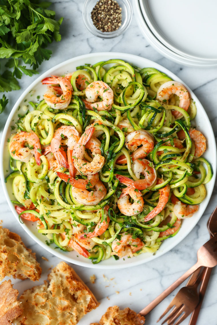 Shrimp with zucchini noodles tossed in herbs on a white plate with parsley and crusty bread nearby