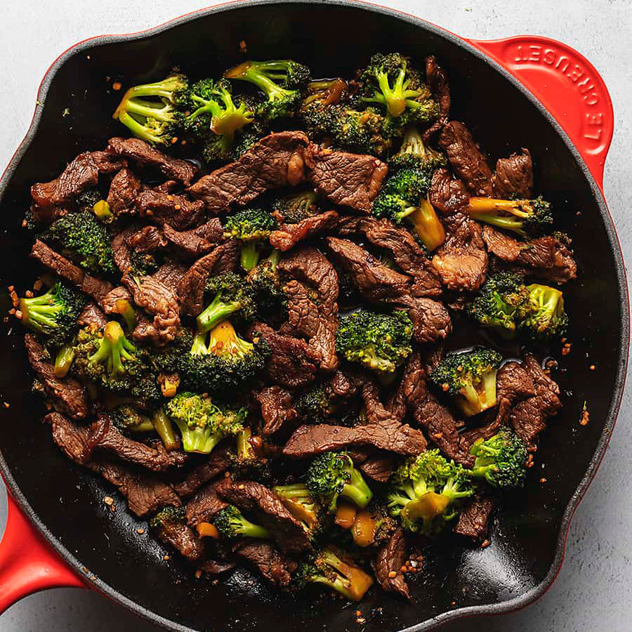 Beef and broccoli stir fry in a dark skillet with a red handle
