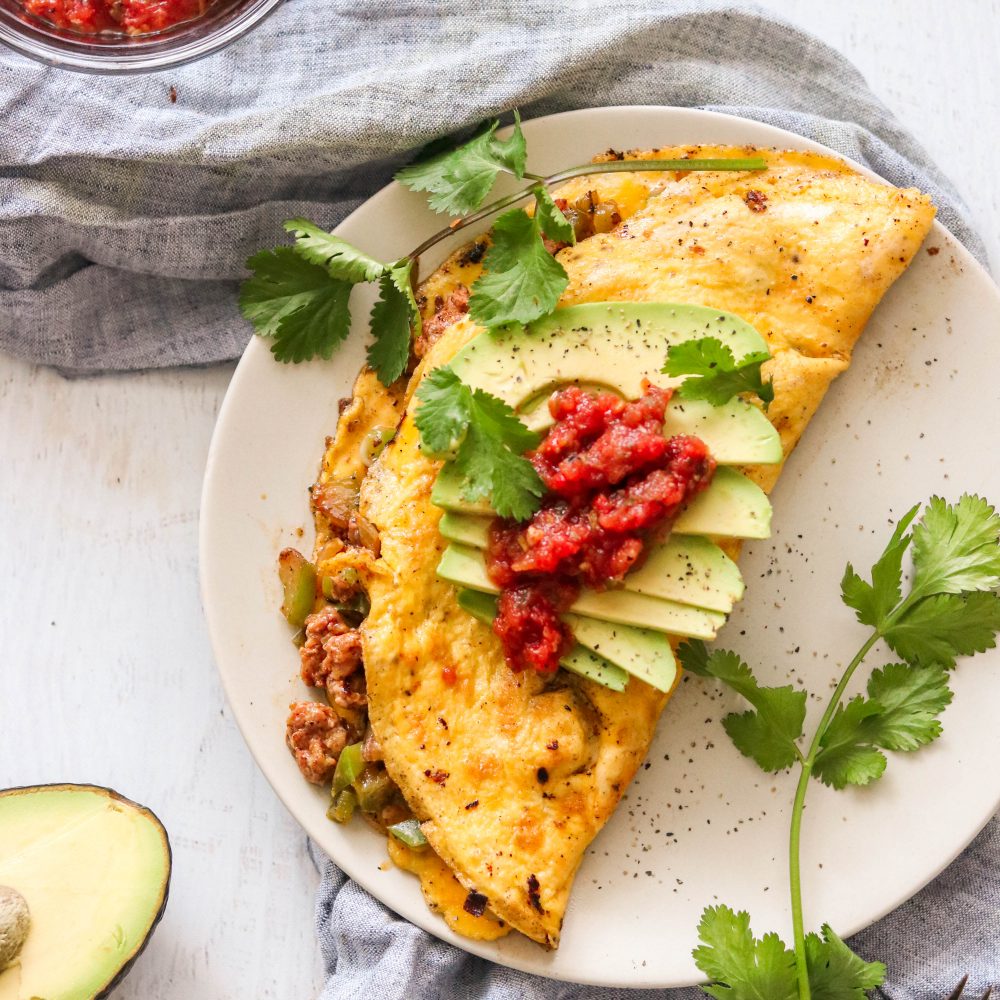 Keto chorizo omelette with avocado slices and cilantro on a white plate.
