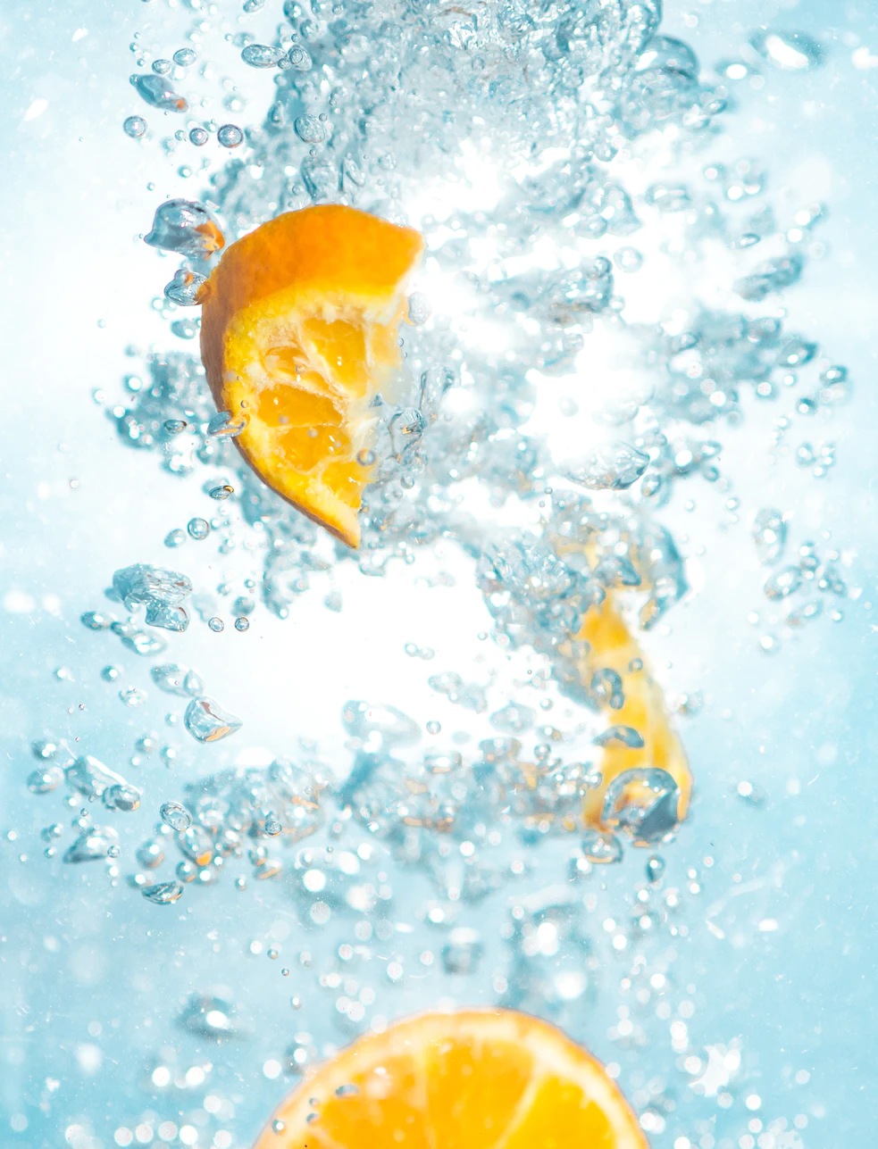 Lemon wedges plunged into sparkling blue water with bubbles rising.