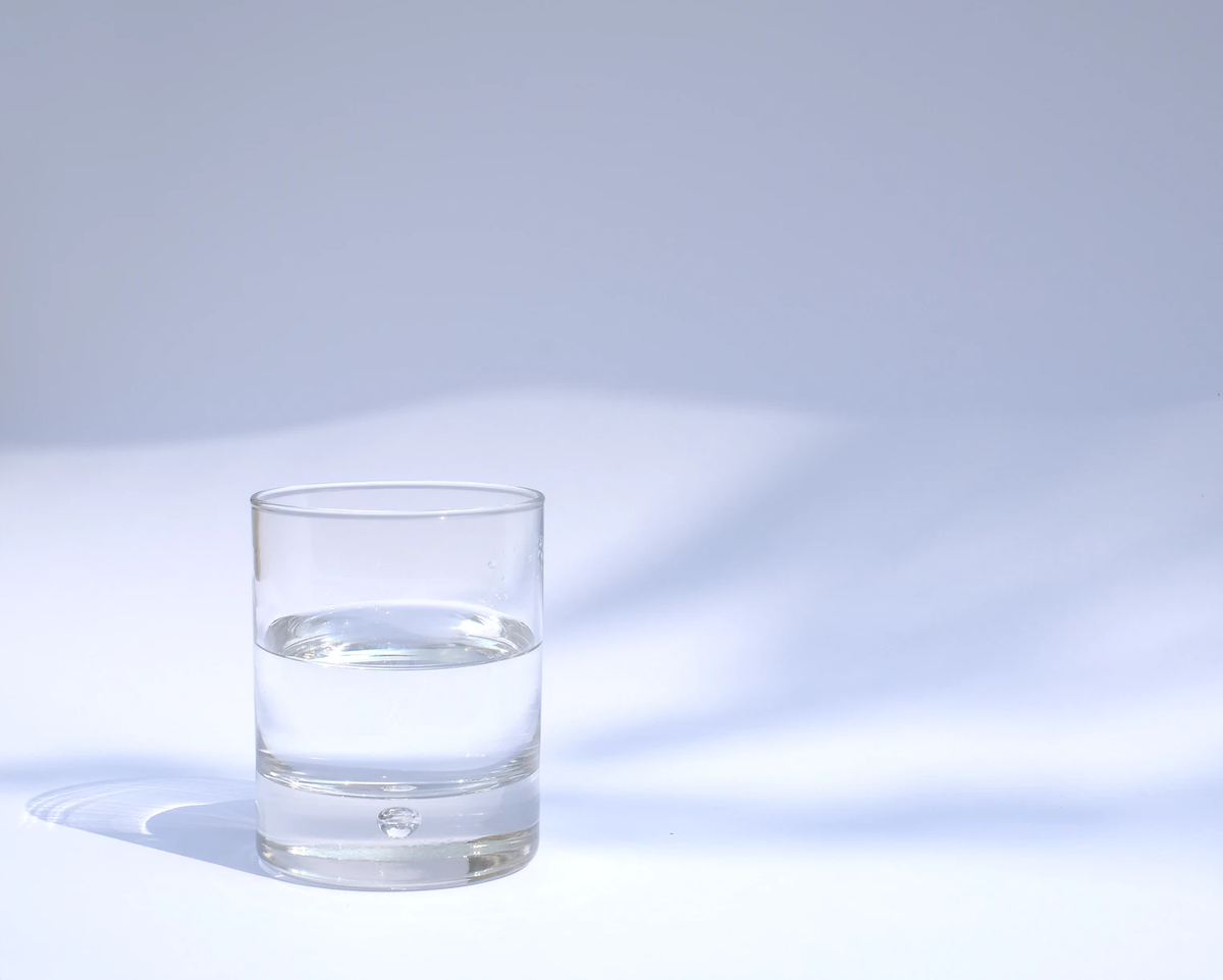 Clear glass of water on a white surface with a soft blue background.
