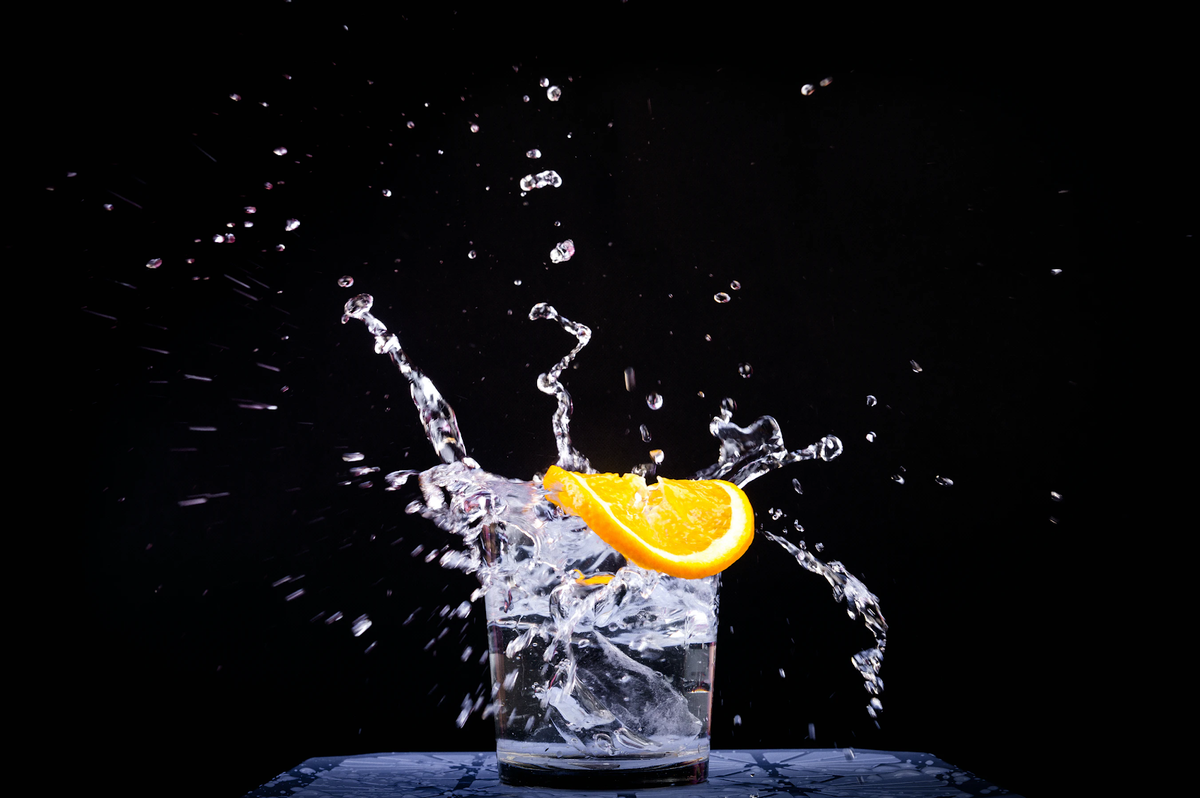 Orange slice in a glass of water as droplets splash against a black background.