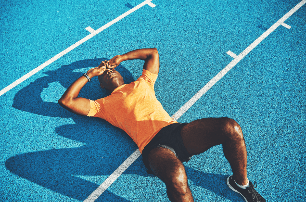 Athlete resting on a blue running track after a workout.