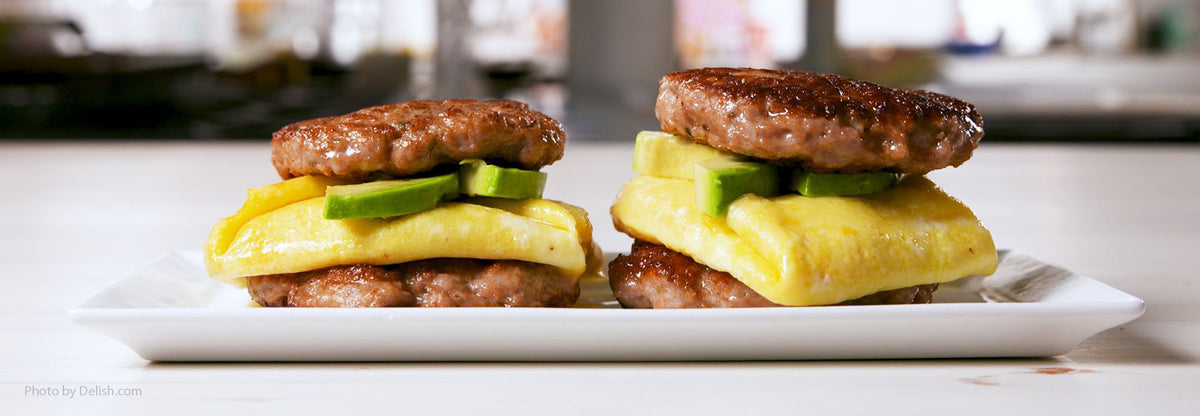 Two keto breakfast sandwiches with beef patties folded eggs and avocado on a white plate