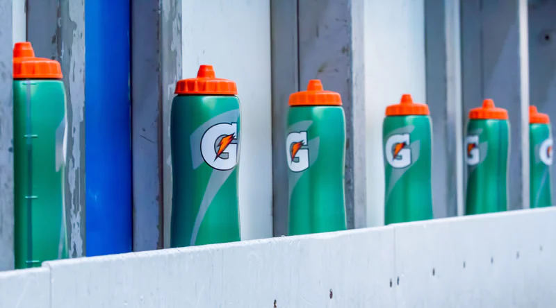 Row of green sports drink bottles with orange caps lined up on a bench