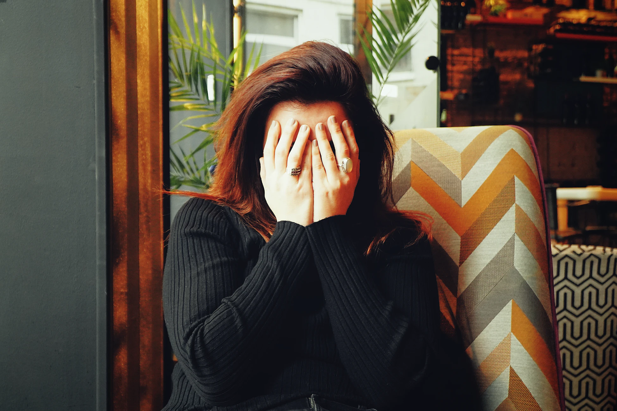 Woman in a black sweater covers her face with both hands while sitting on a chevron patterned chair