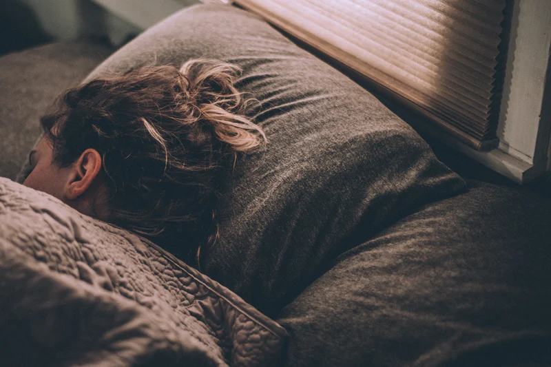 Person sleeping in a dimly lit bedroom under a blanket.
