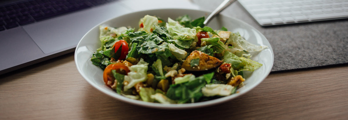 Low carb taco salad with greens cherry tomatoes and corn in a white bowl on a desk with a laptop in the background