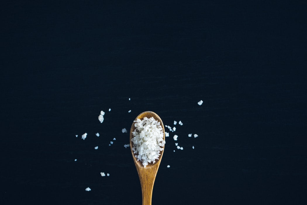 Wooden spoon filled with coarse salt crystals scattered on a dark surface