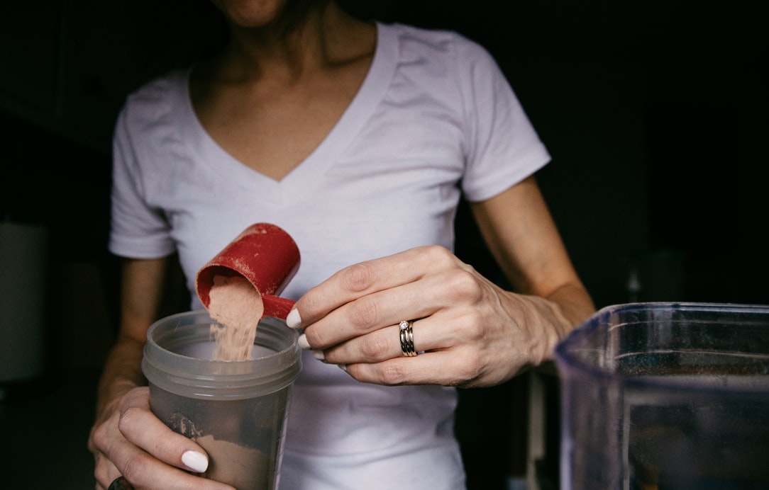 Woman in a white shirt pours protein powder into a shaker bottle